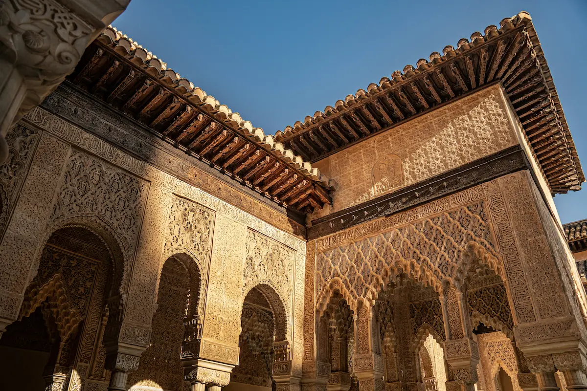 Ornate arches in Alhambra Palace, Spain, overlooking an inner courtyard with lush gardens and reflective pools.