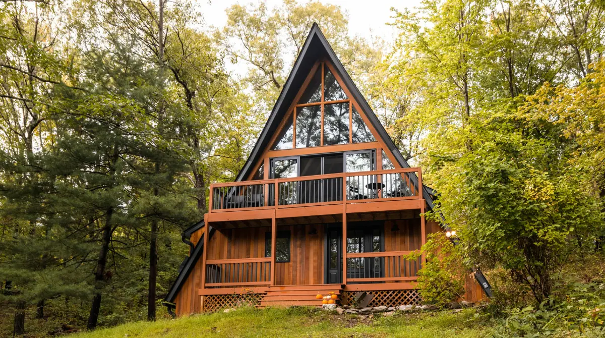 Brown wooden house on a hill with a unique modern roof, surrounded by trees.