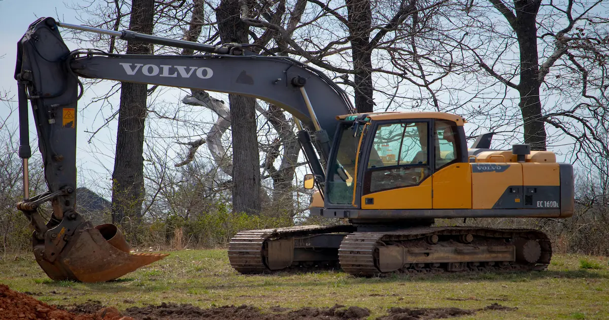 yellow and black excavator on a green field near leafless trees used for foundation excavation