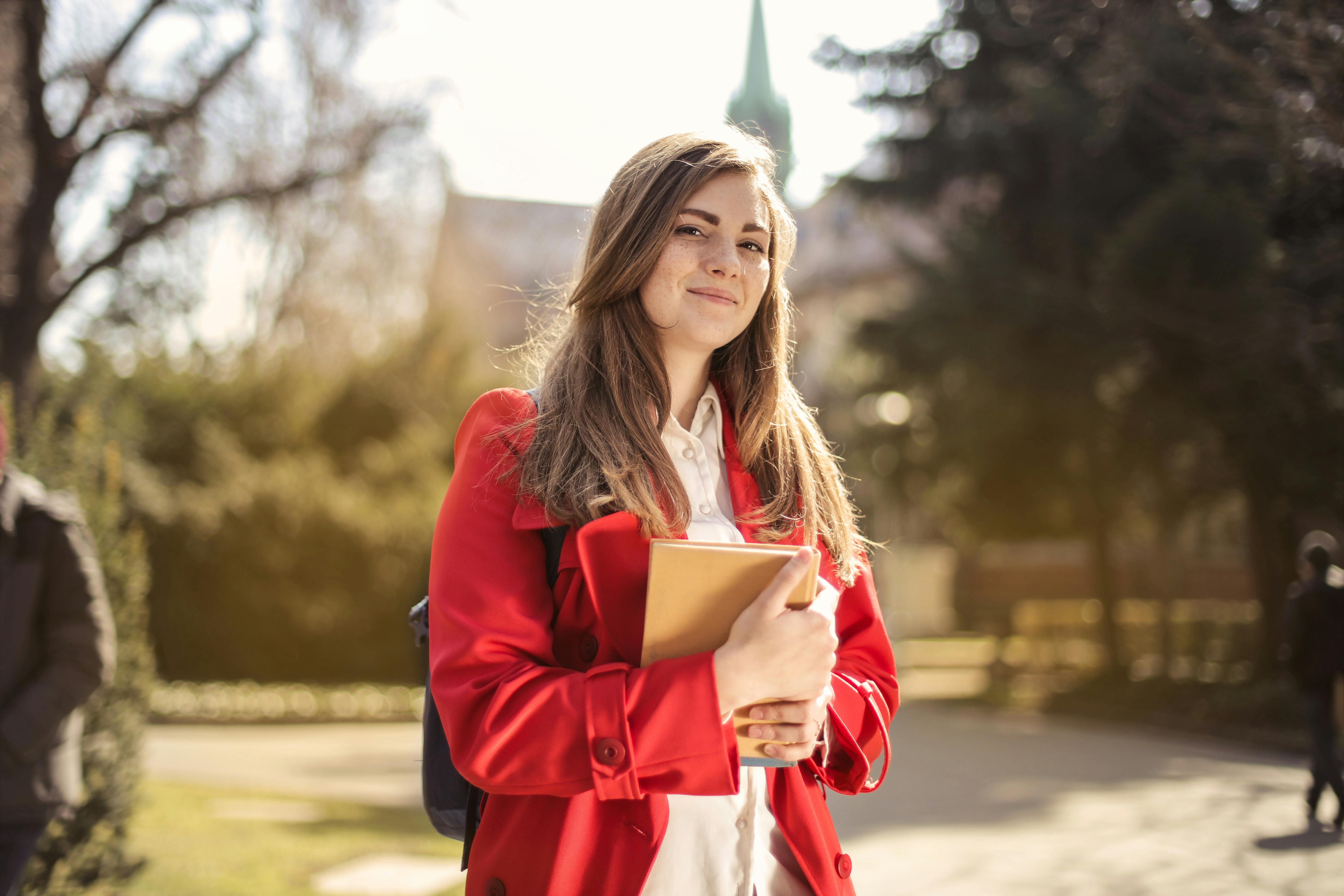 Architecture student standing proudly in front of university with portfolio in hand.