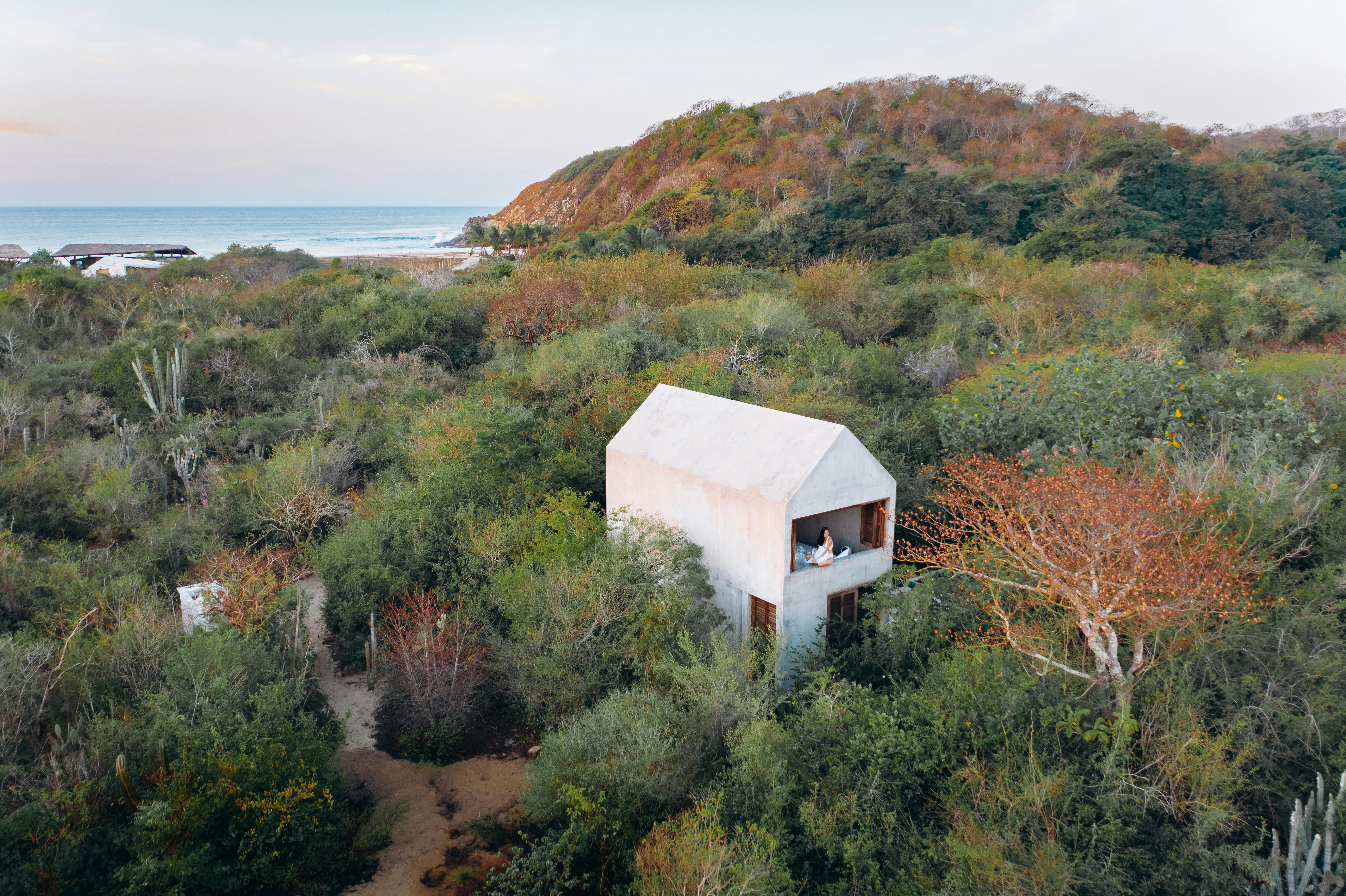 Small modern white wooden house on grass field near water in Mexico.