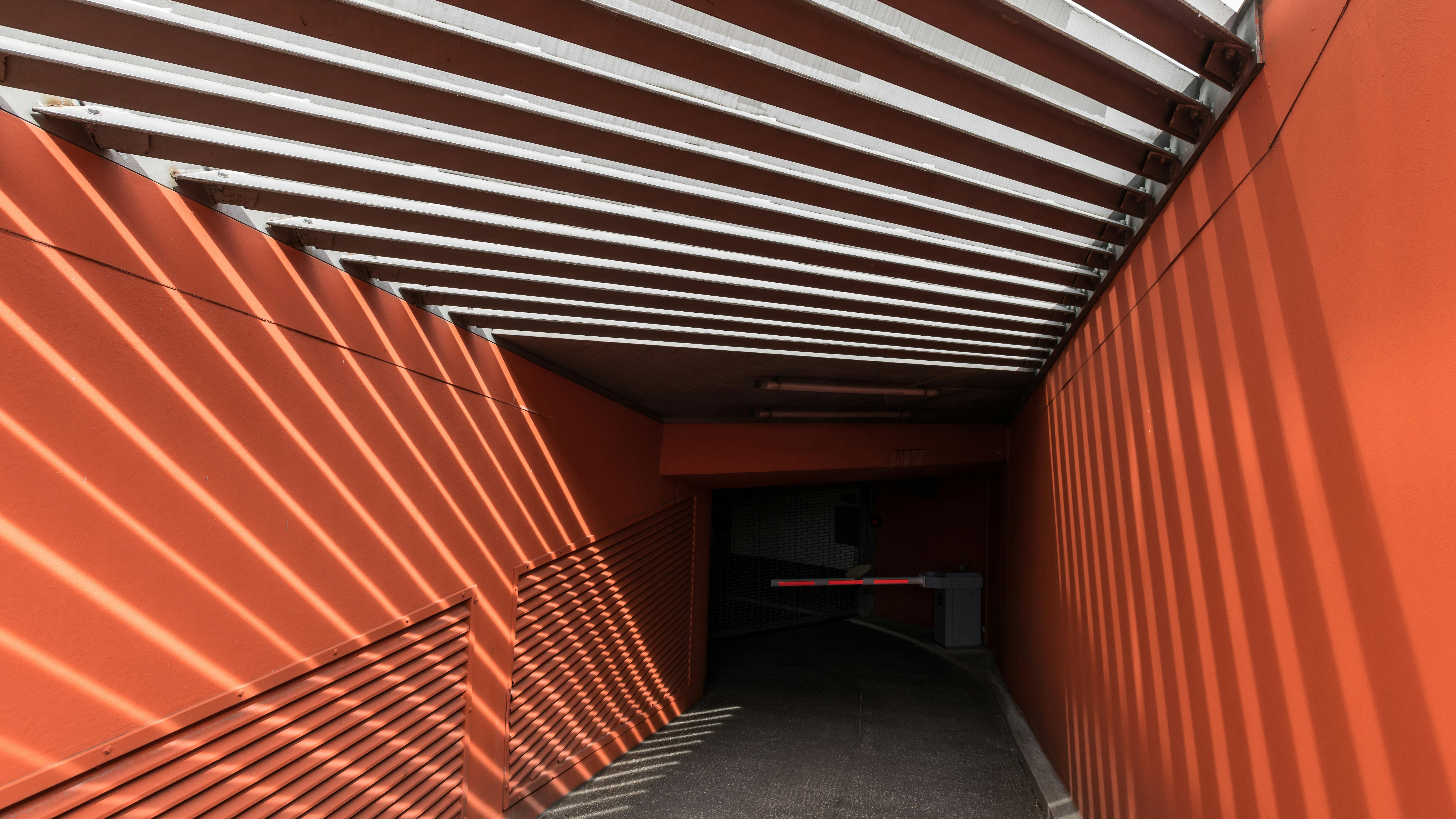 A tunnel in Hamburg with terracotta orange walls, where sunlight filters through white beams, casting striped shadows that highlight the warm earthy tones and depth of the architecture.