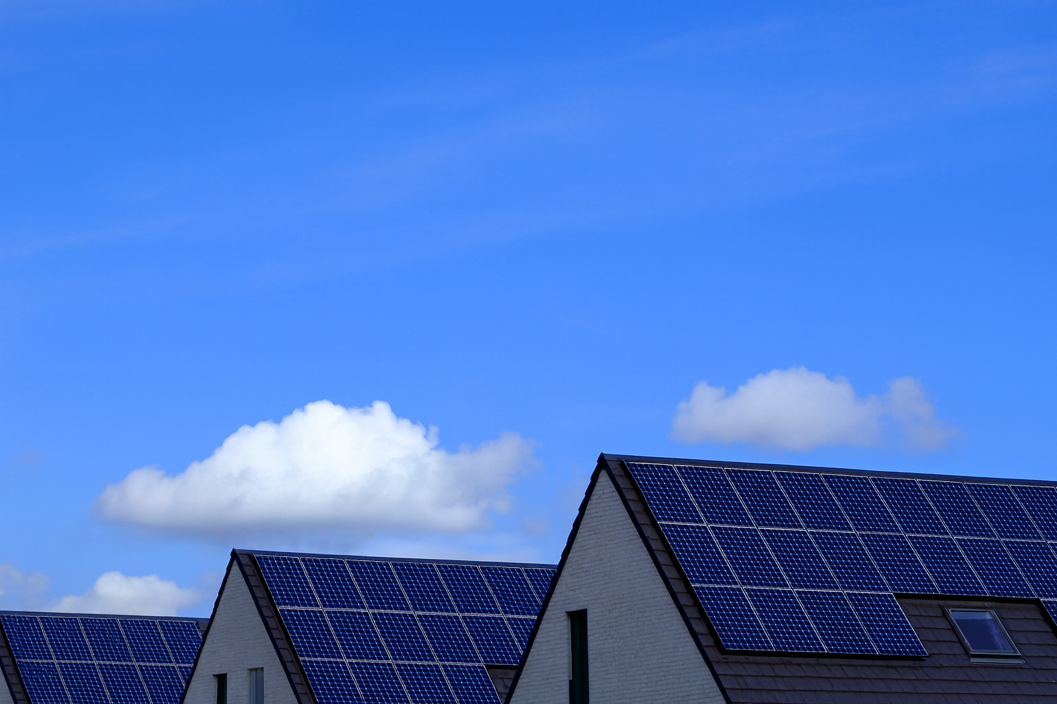 Row of modern gable-roof houses with solar panels under a bright blue sky with clouds.