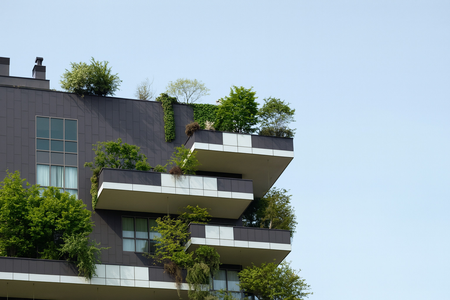 Contemporary high-rise with layered balconies featuring lush plants and trees.