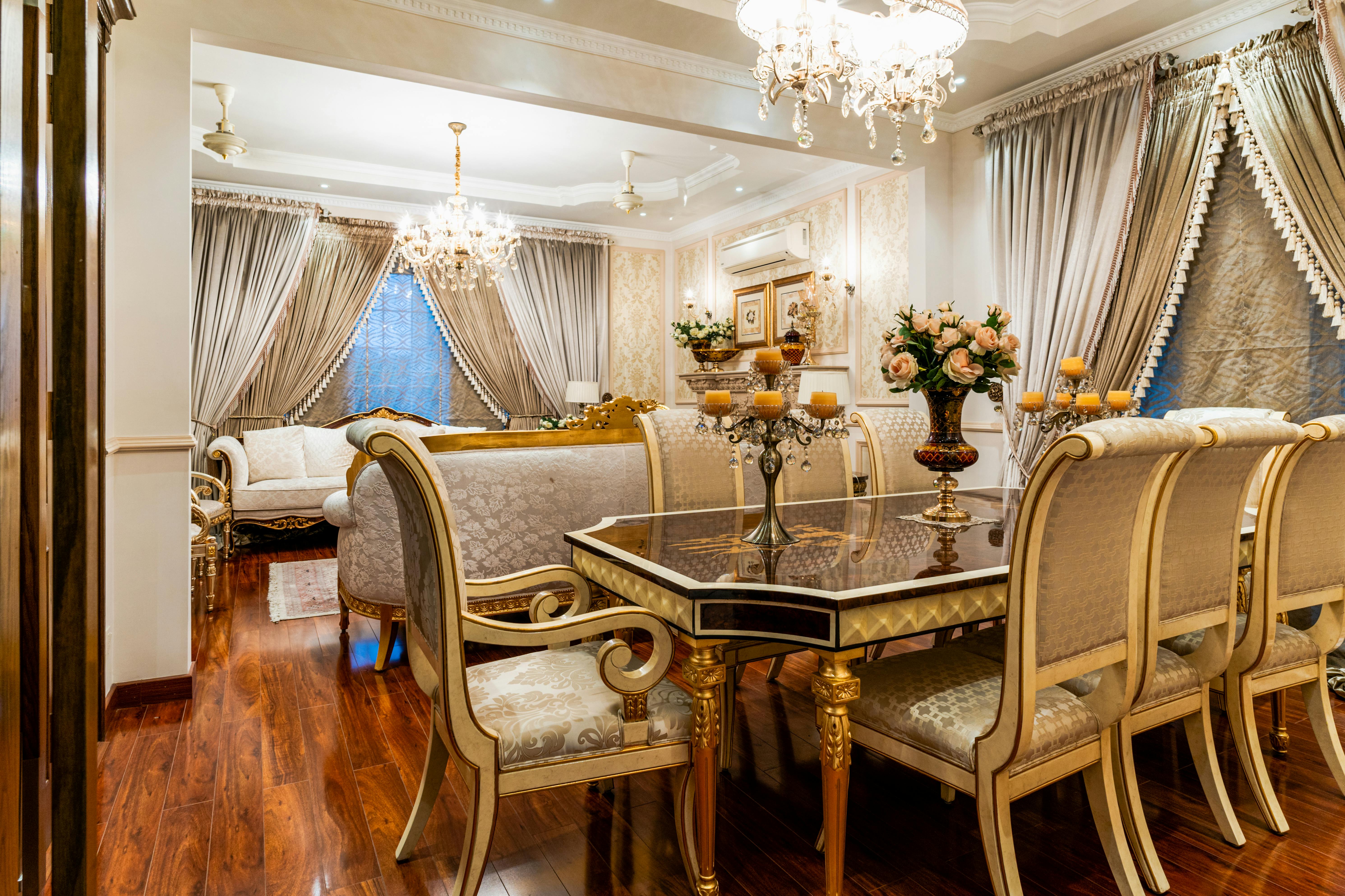 Luxurious traditional American dining room with gold-accented furniture, crystal chandeliers, and detailed drapery.