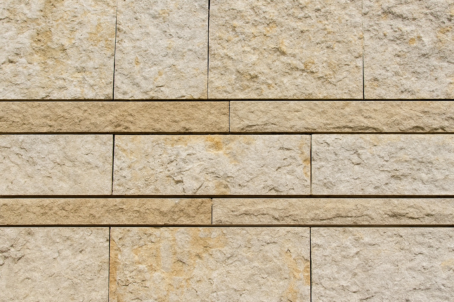 Beige natural stone wall with two horizontal dividing stripes and textured surface.