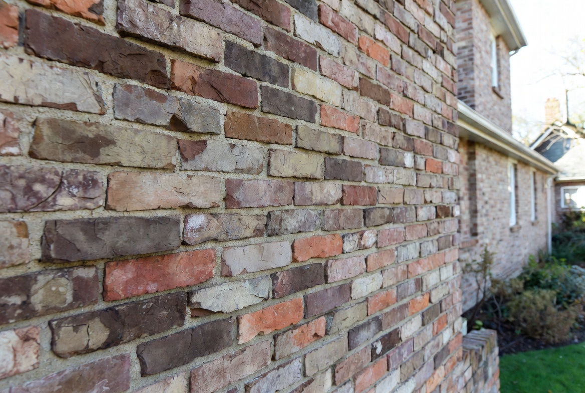 Antique thin brick veneer on modest residential house exterior with reclaimed weathered texture .