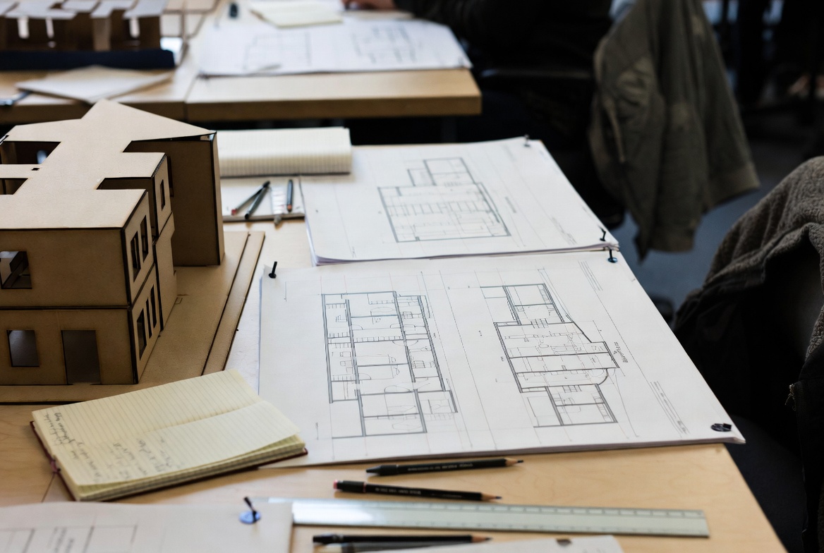 Architecture project work with floor plan sheets, model study, and drafting tools on a desk.
