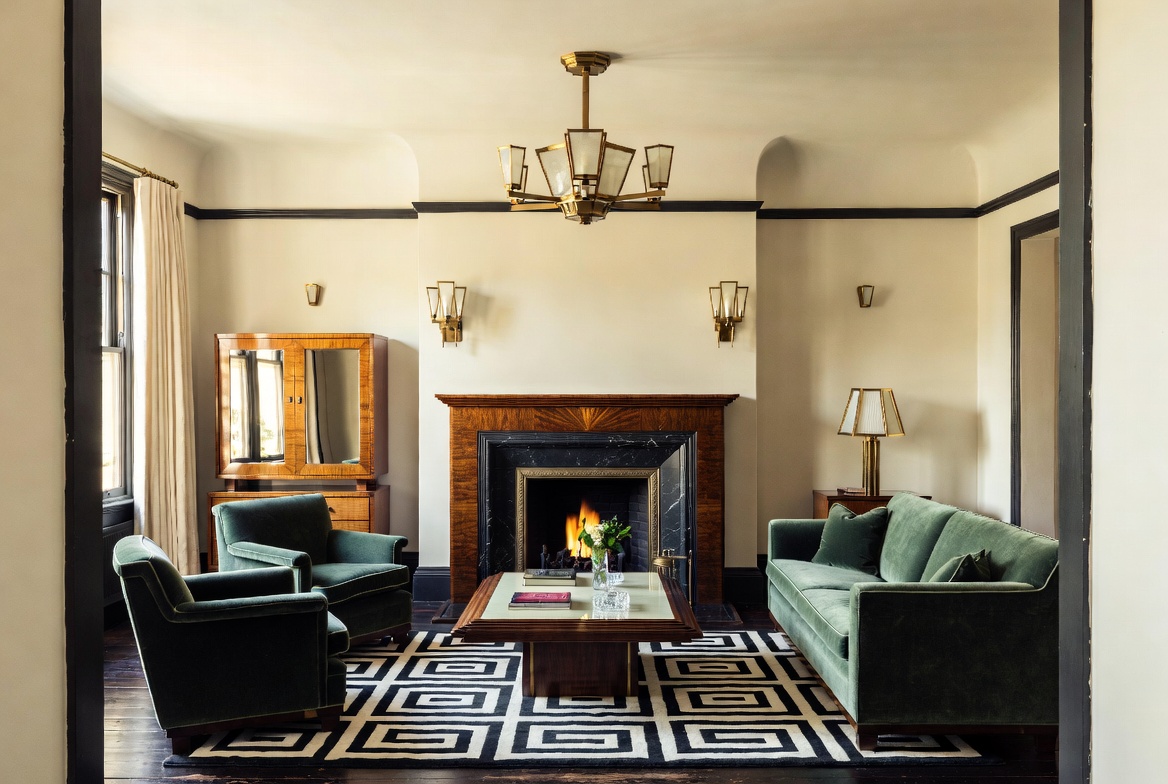 Art Deco sitting room with stepped wall geometry, polished wood paneling, symmetrical lighting, and a sunburst fireplace design.