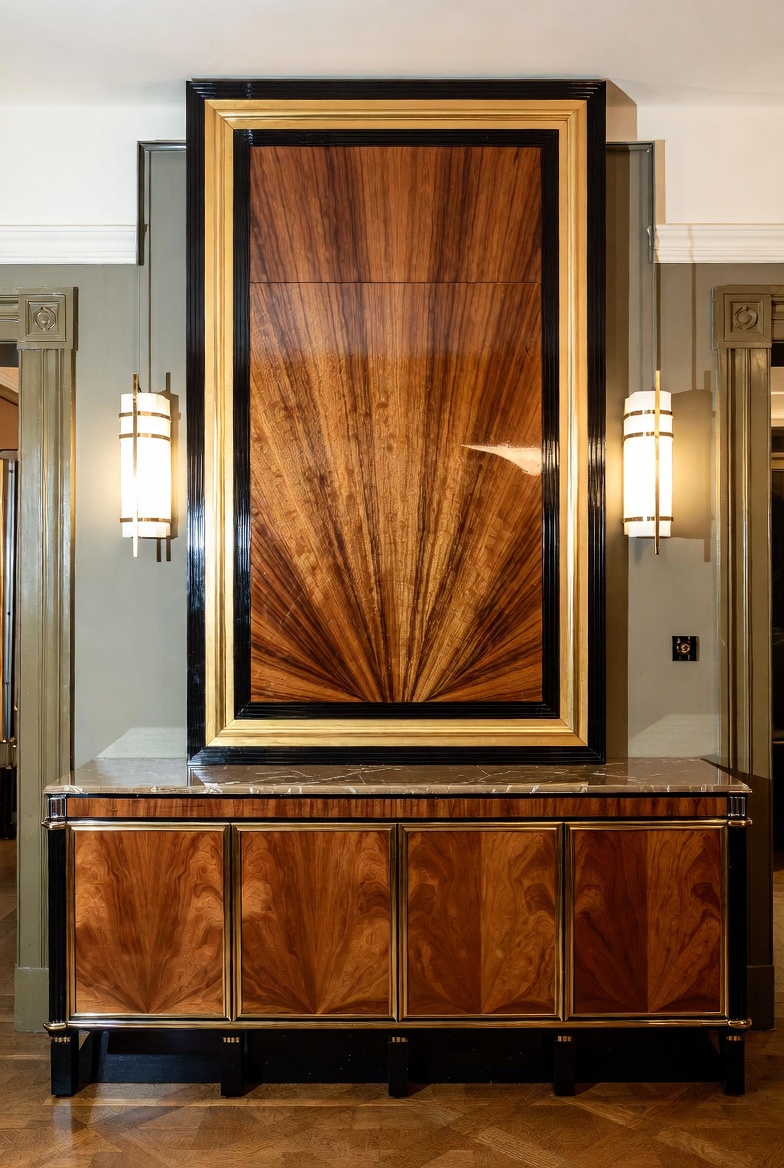 Art Deco veneer panel with sunburst wood grain, black lacquer framing, and flanking wall sconces.