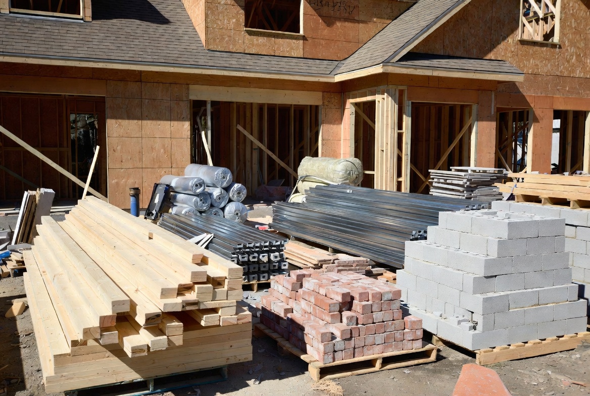 Common building materials including lumber, brick, concrete block, steel, and insulation at a residential jobsite.