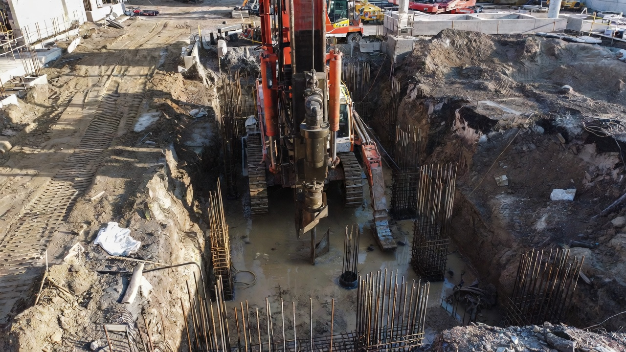 Deep foundation excavation with drilling rig installing drilled pier foundations and rebar cages.