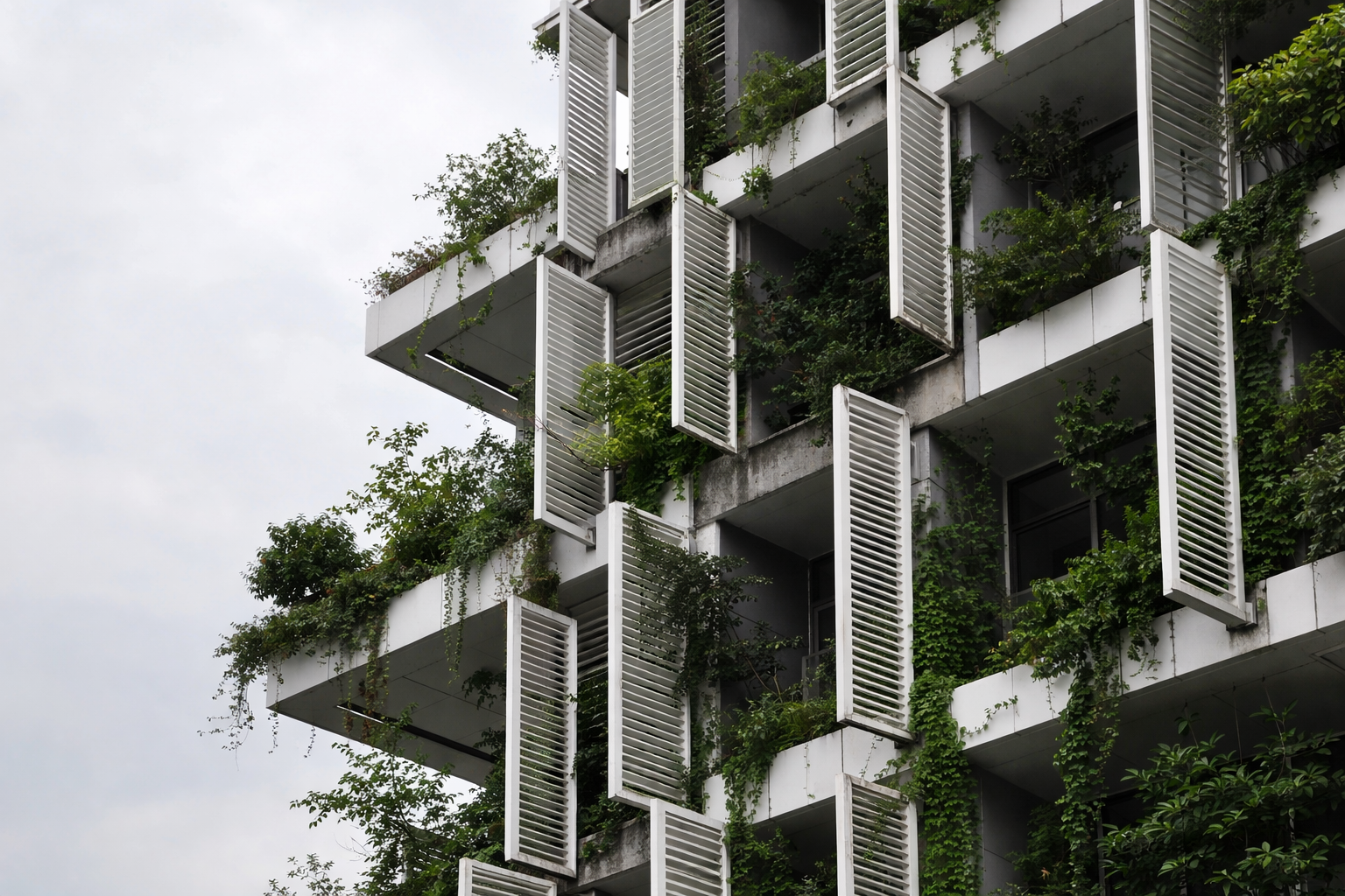 Modern building with vertical louvers and balcony greenery on a concrete facade.