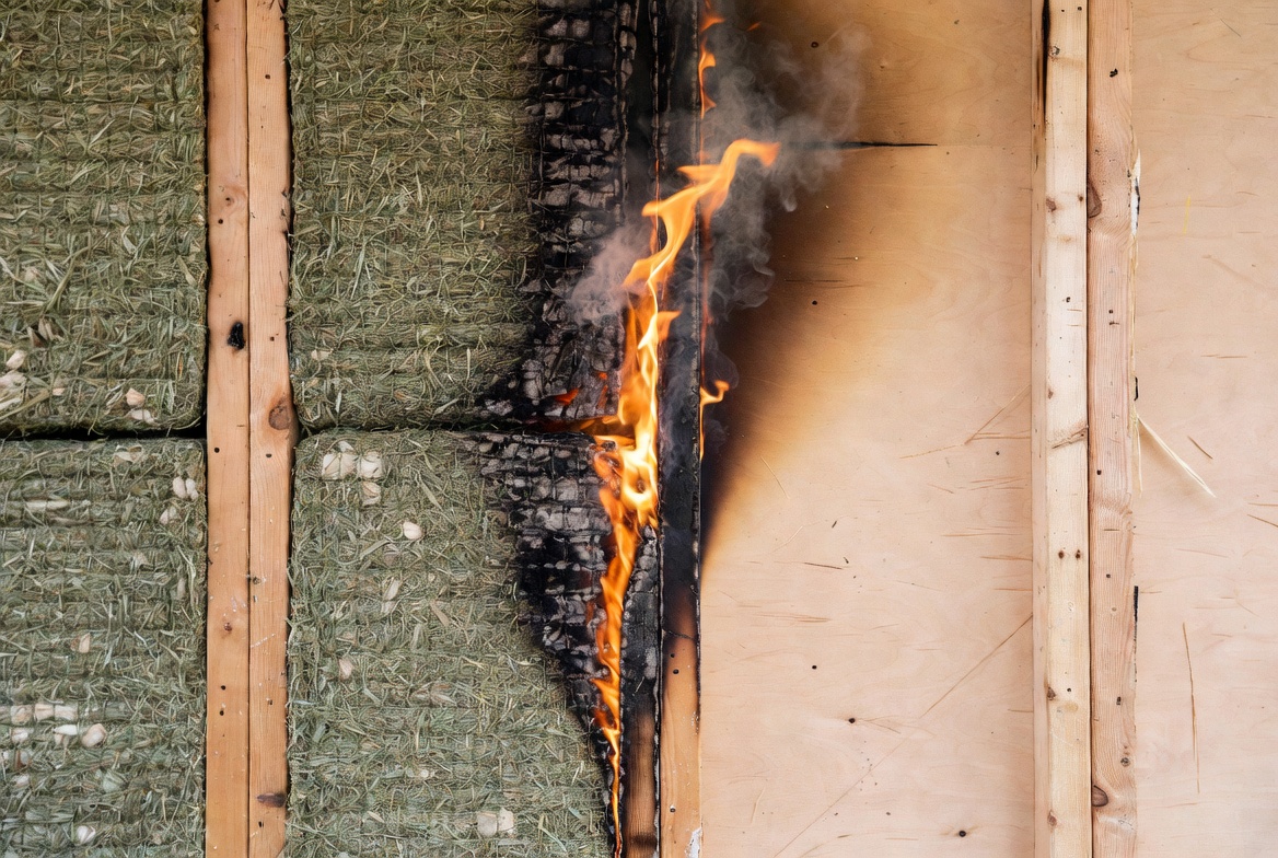 Hemp insulation in an open stud wall showing flame exposure, surface charring, and smoke.