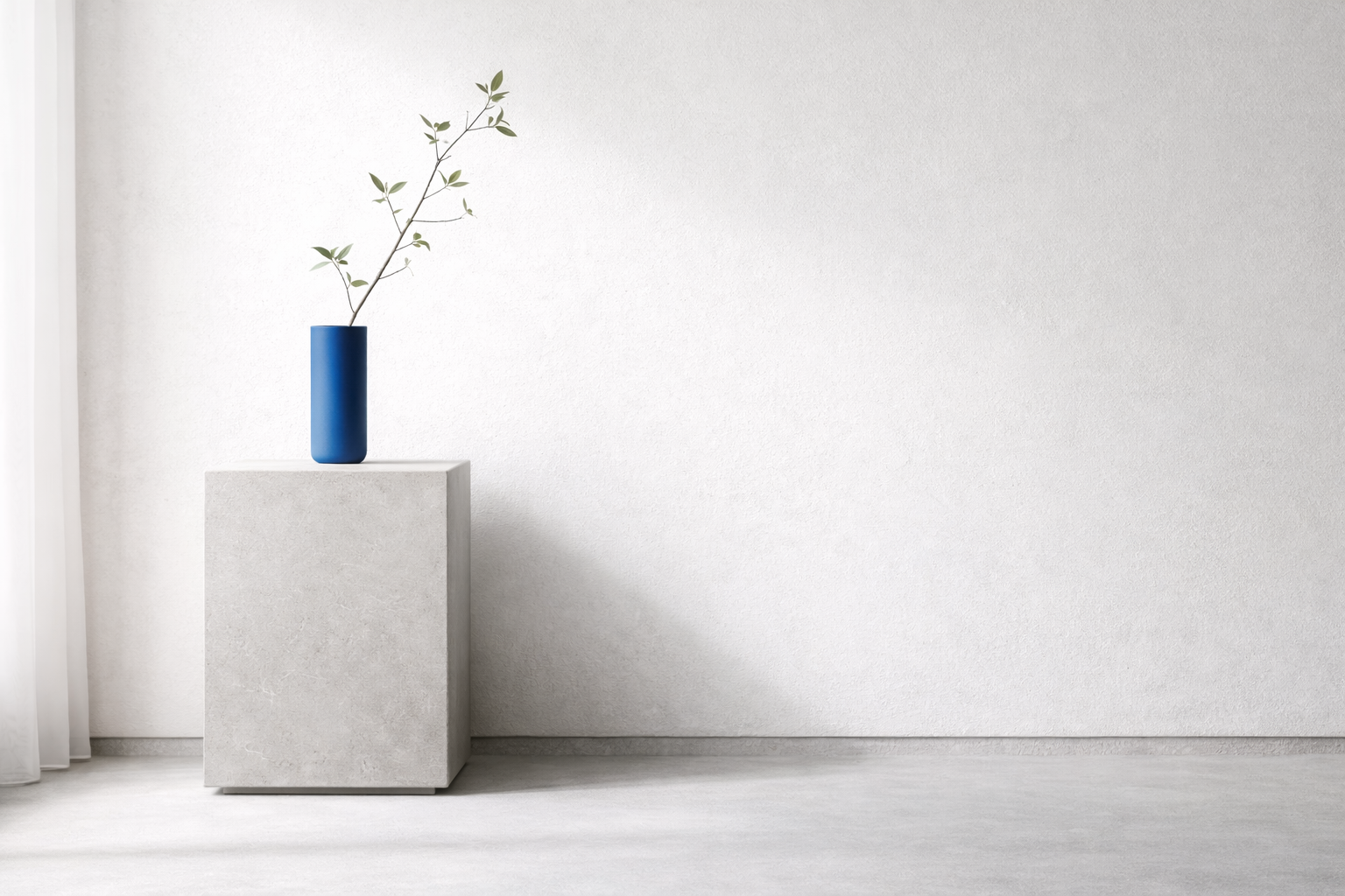 Cobalt blue vase on a gray plinth with a single branch against a light wall.