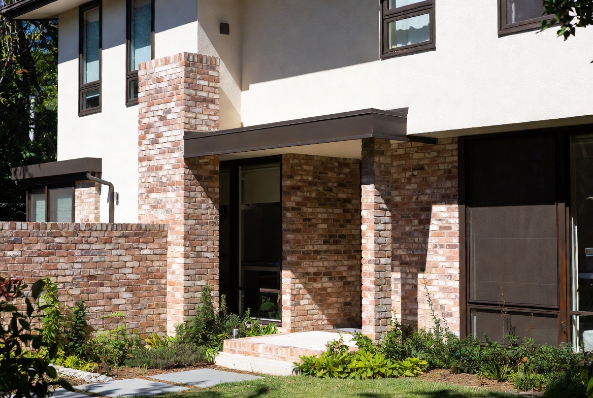 Modern house entry with brick accent walls, chimney, and restrained landscaping.