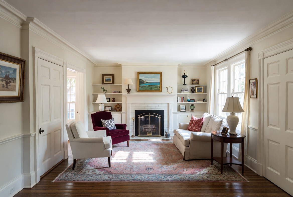 Traditional American living room with fireplace, symmetrical furniture, hardwood floors, and a rug with classic trim and decor.