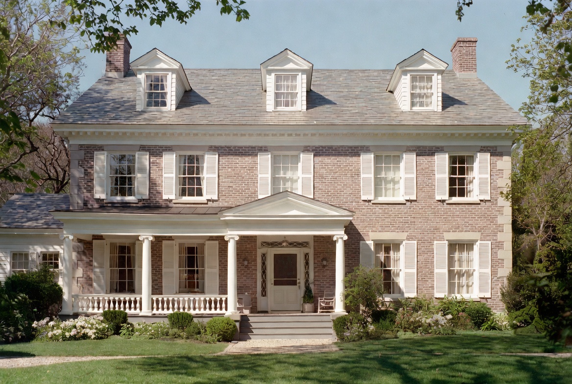 1910s Colonial Revival house with brick facade, dormers, shutters, and a classical front porch.