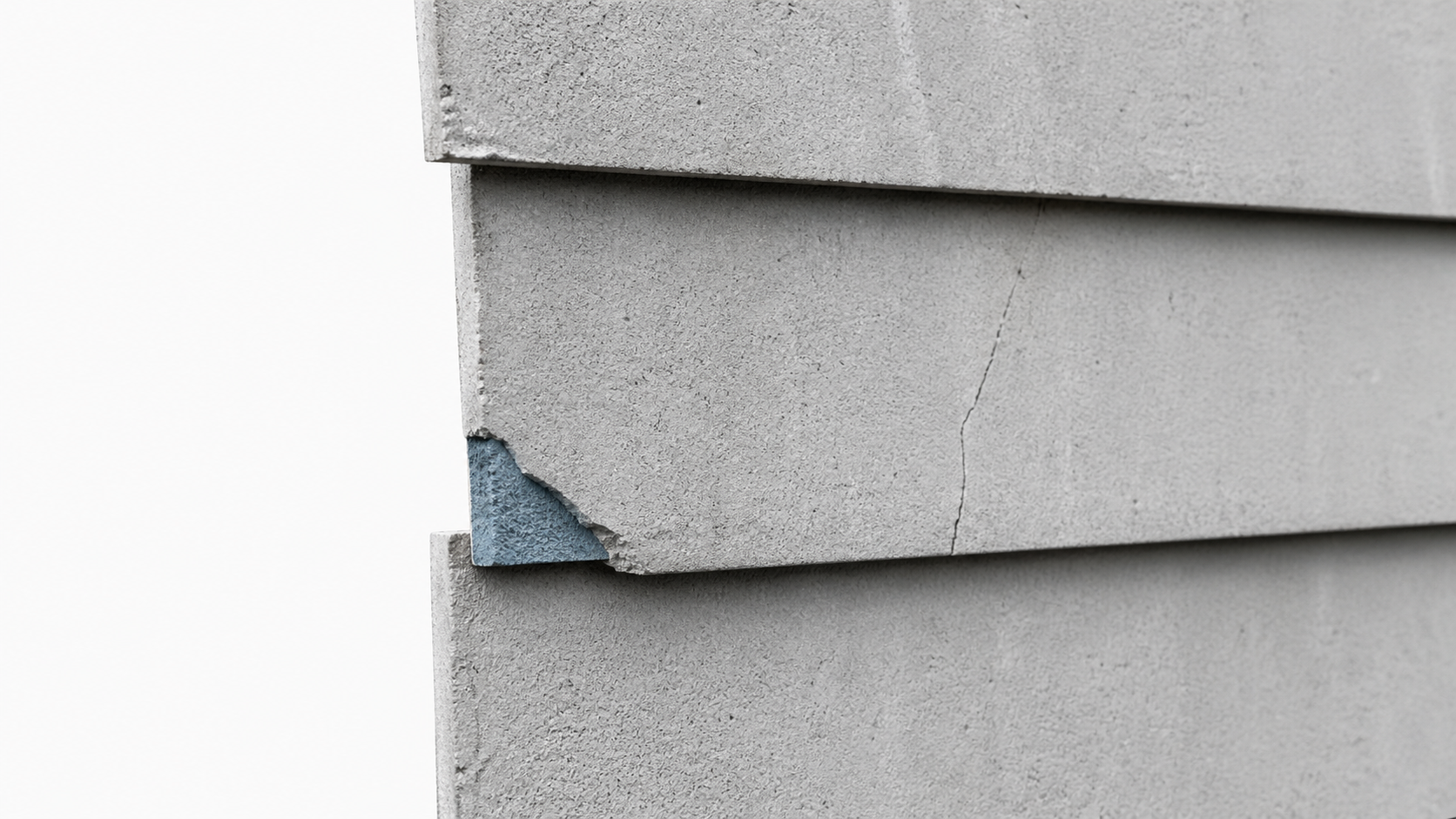 Close detail of old asbestos cement siding with overlapping courses, a chipped corner, and a hairline crack.