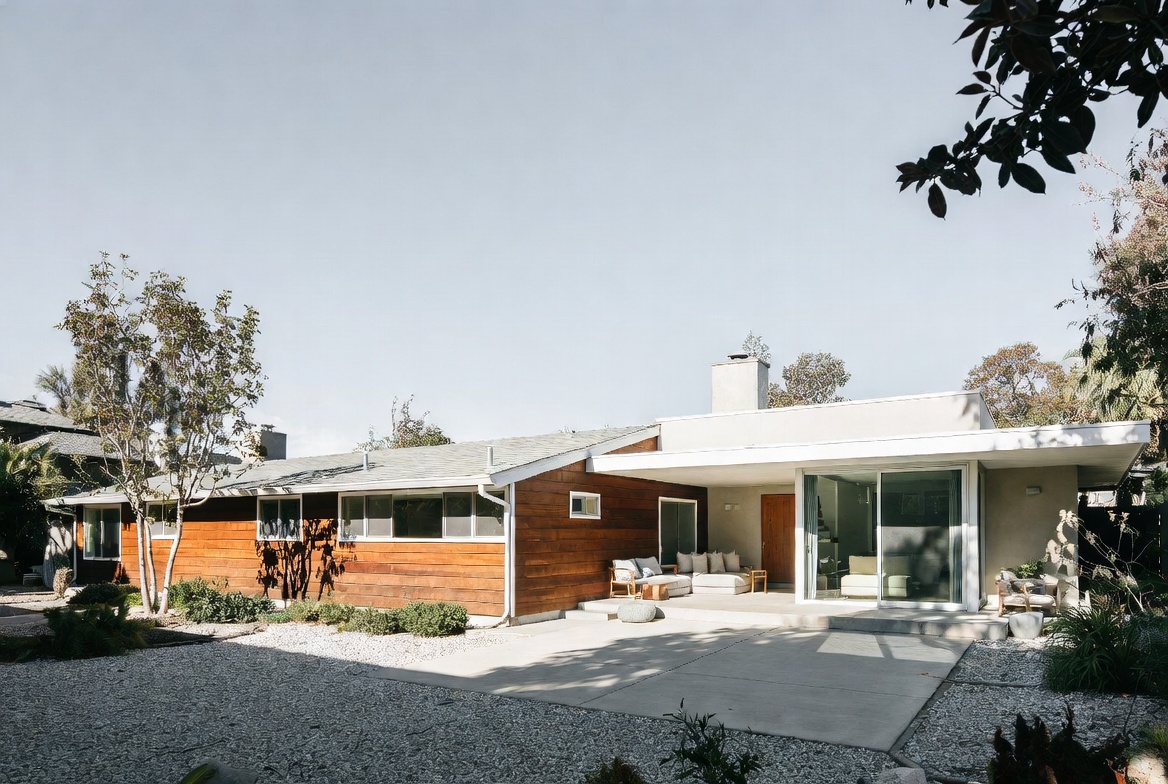 Rear addition to a ranch house with a wood-clad volume, modern patio, and large glass opening.