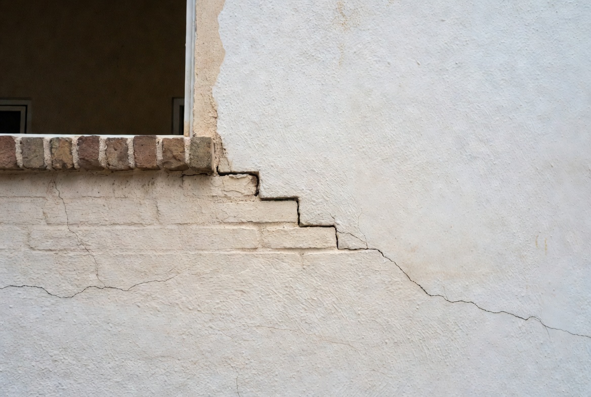 Close view of a stair-step settlement crack beneath a window in a stucco wall.