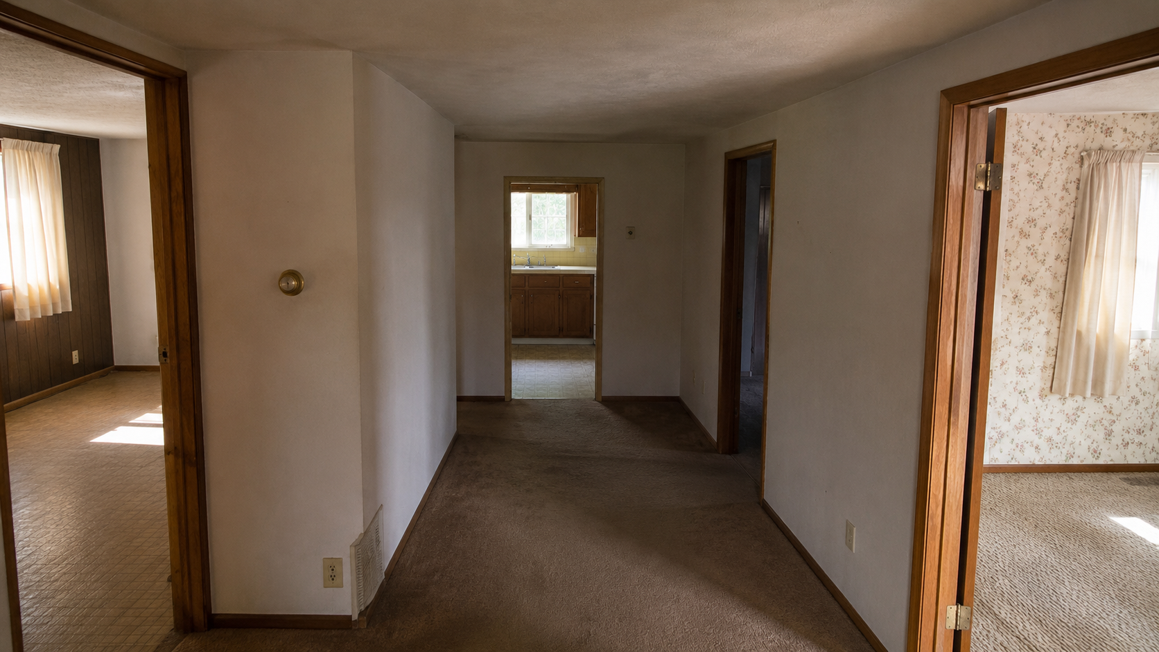 Older ranch house interior with a dark central hallway, low ceiling, small room openings, and limited natural light before renovation.