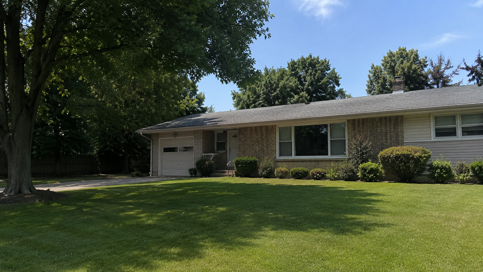 Typical 1950s ranch house with low roofline, brick and siding exterior, attached garage, picture window, lawn, and shrubs.