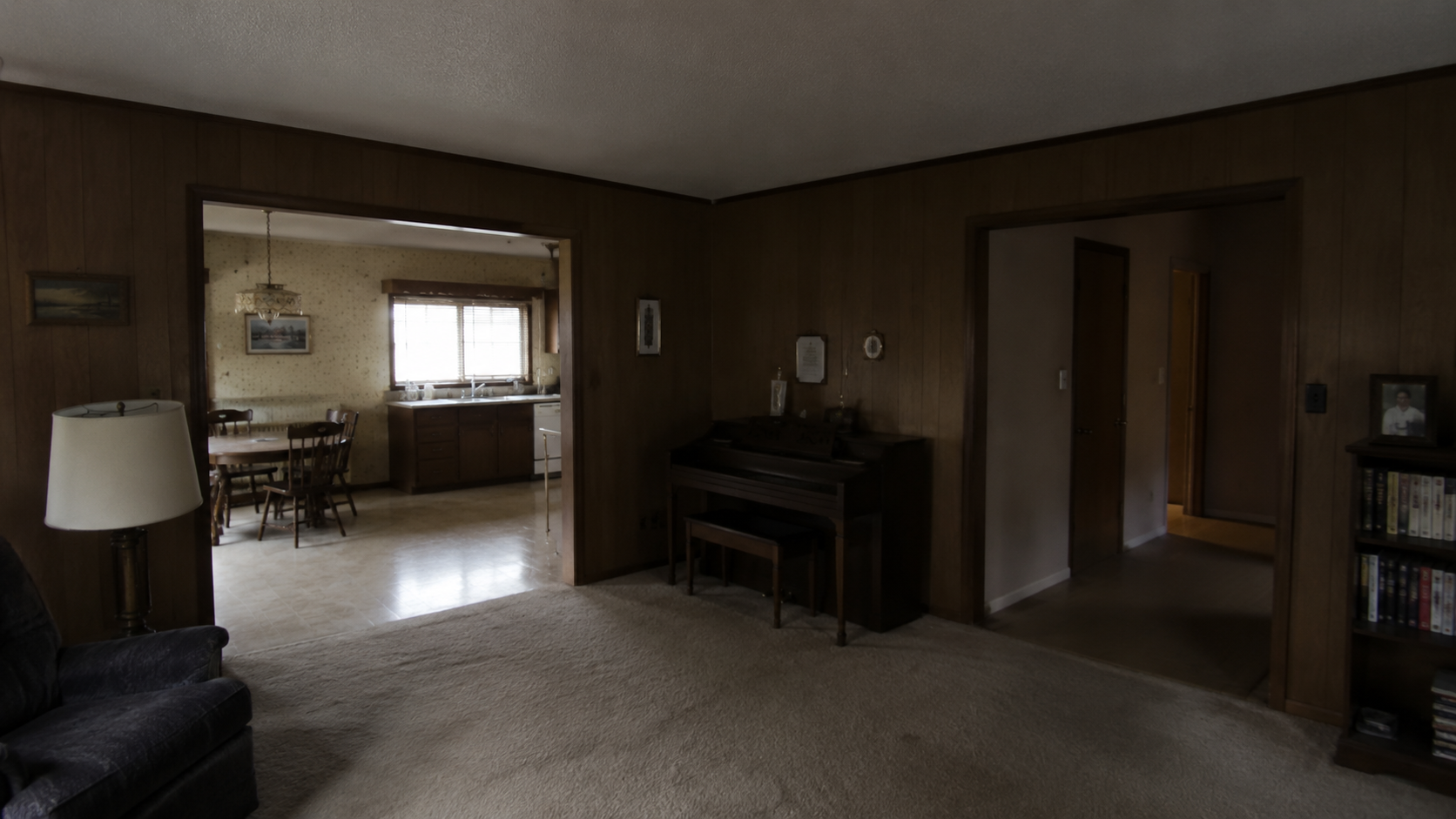 Dark middle room in a 1960s ranch house with wood paneling, low ceiling, and limited natural light.