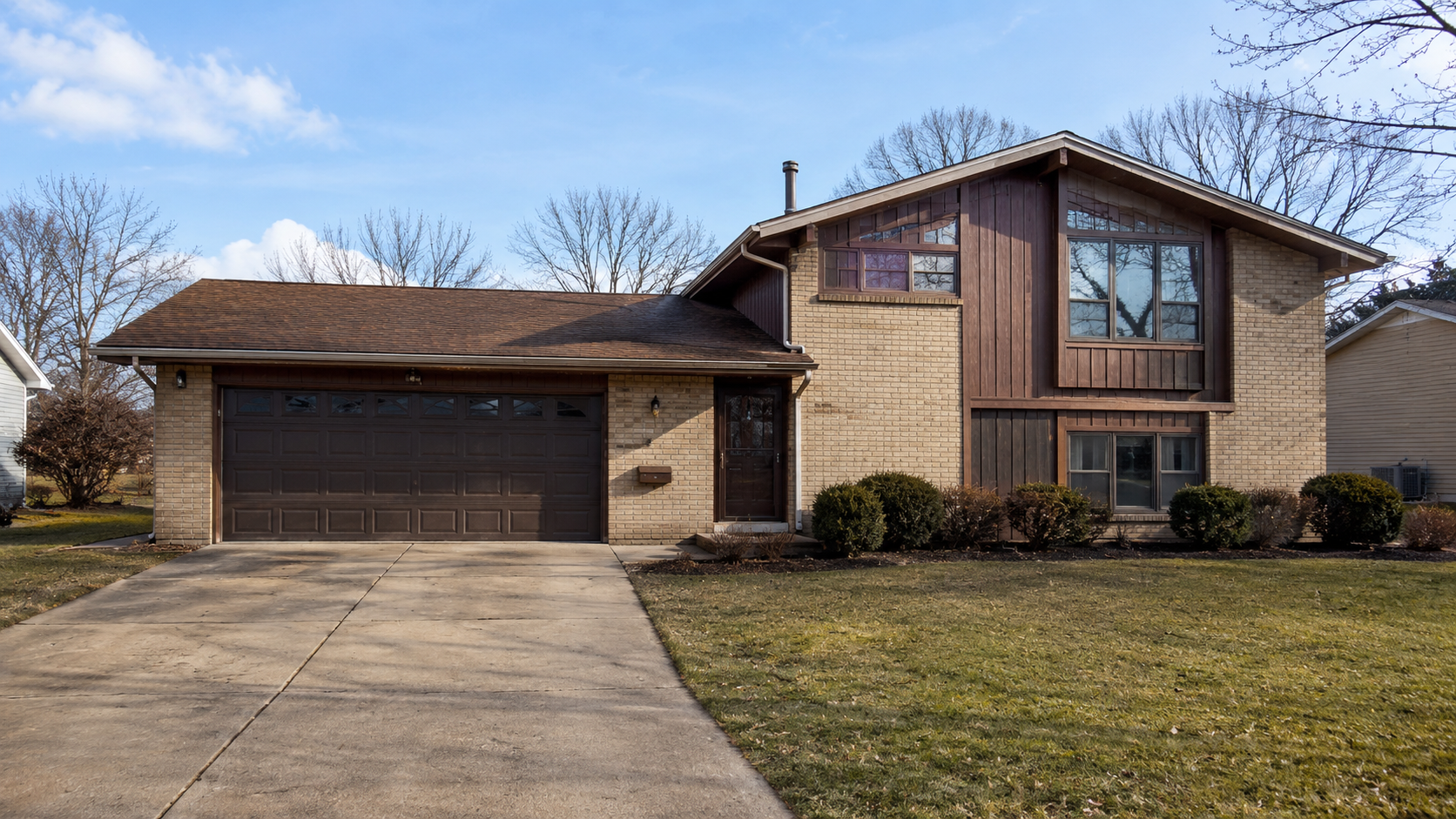 1970s split-level suburban house with brick, vertical wood siding, attached garage, and dated entry.