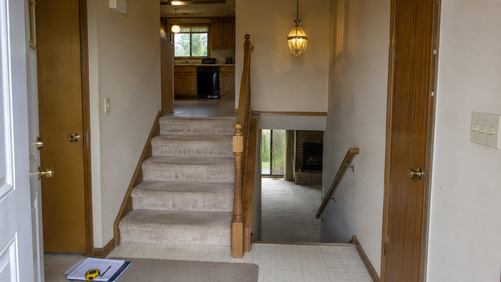 1980s split-level entry with stairs up and down, oak railing, beige carpet, brass light, and renovation notes.