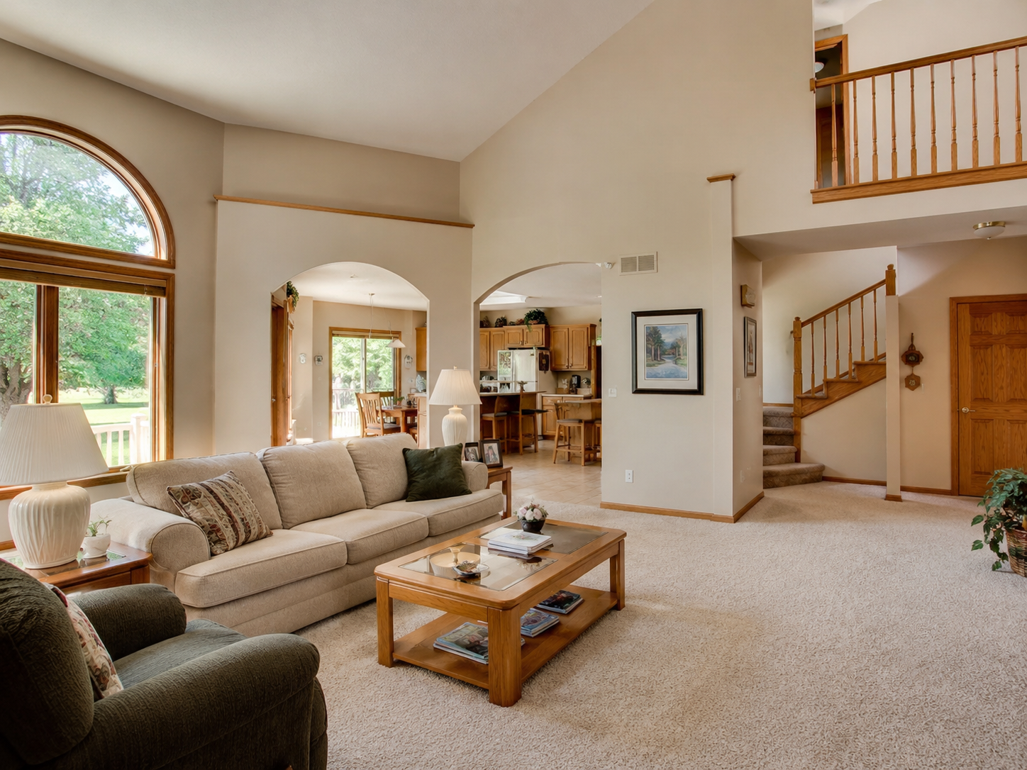 Typical 1990s living room with vaulted ceiling, beige carpet, oak trim, and arched openings.