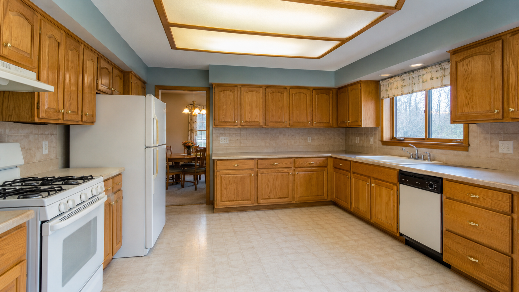 1990s kitchen with honey oak cabinets, laminate counters, white appliances, and dated lighting.