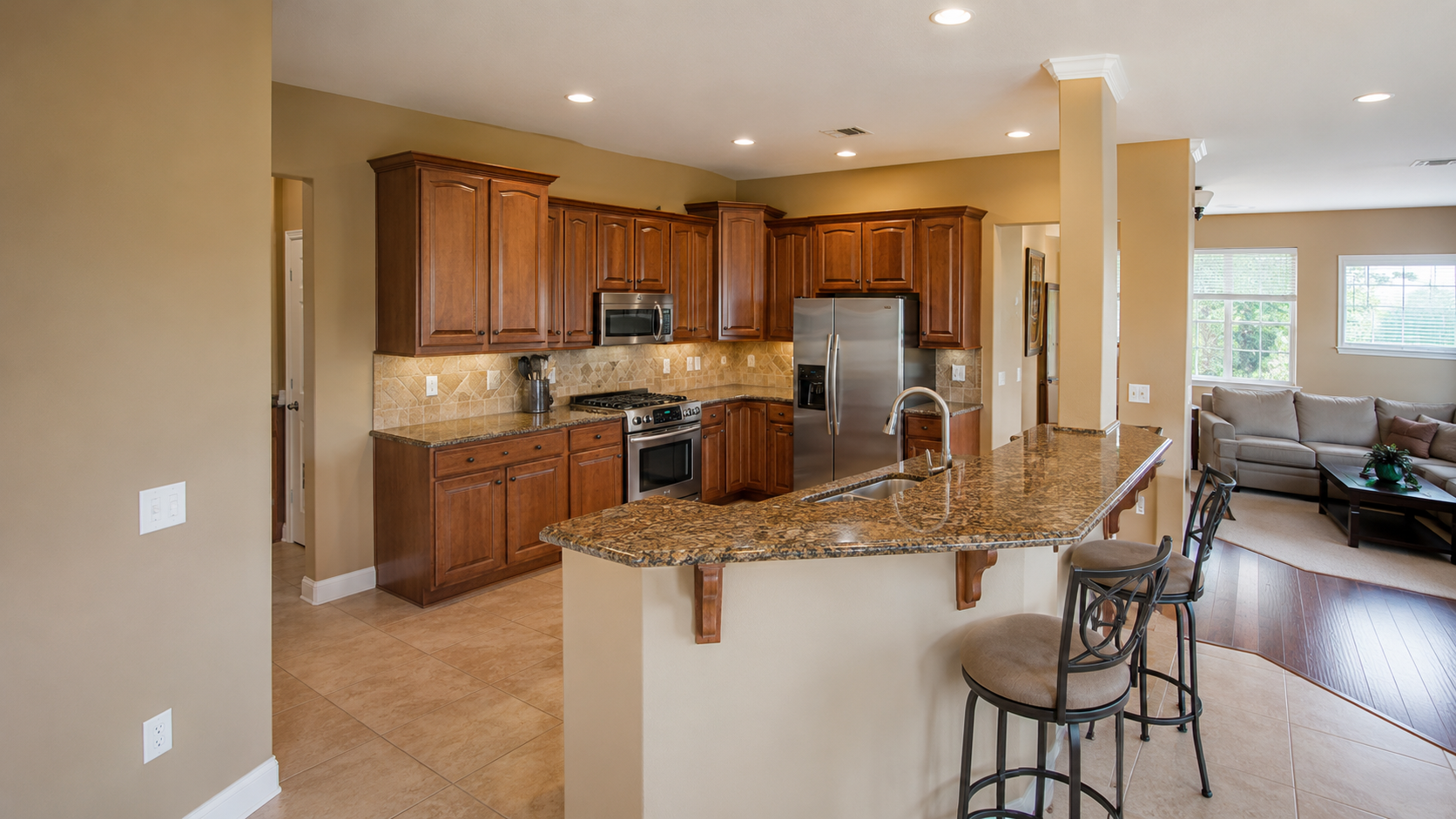 Early 2000s builder kitchen with cherry cabinets, brown granite, tile floor, and open family room.
