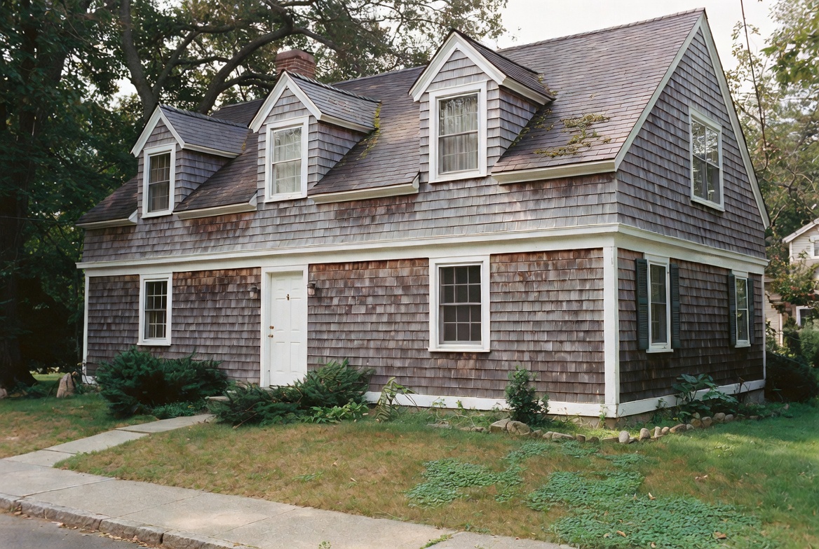 Cape Cod house with weathered shingle siding, dormer windows, and steep roof.