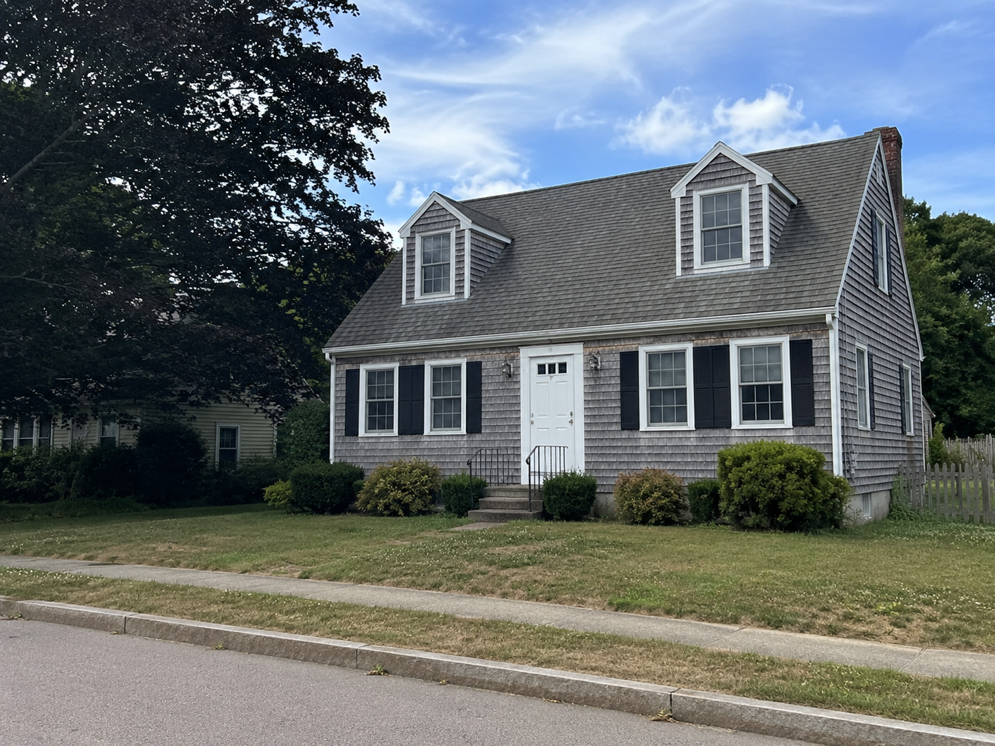 Documentary-style photo of a full Cape Cod house with cedar shakes, dormers, and a simple front facade.