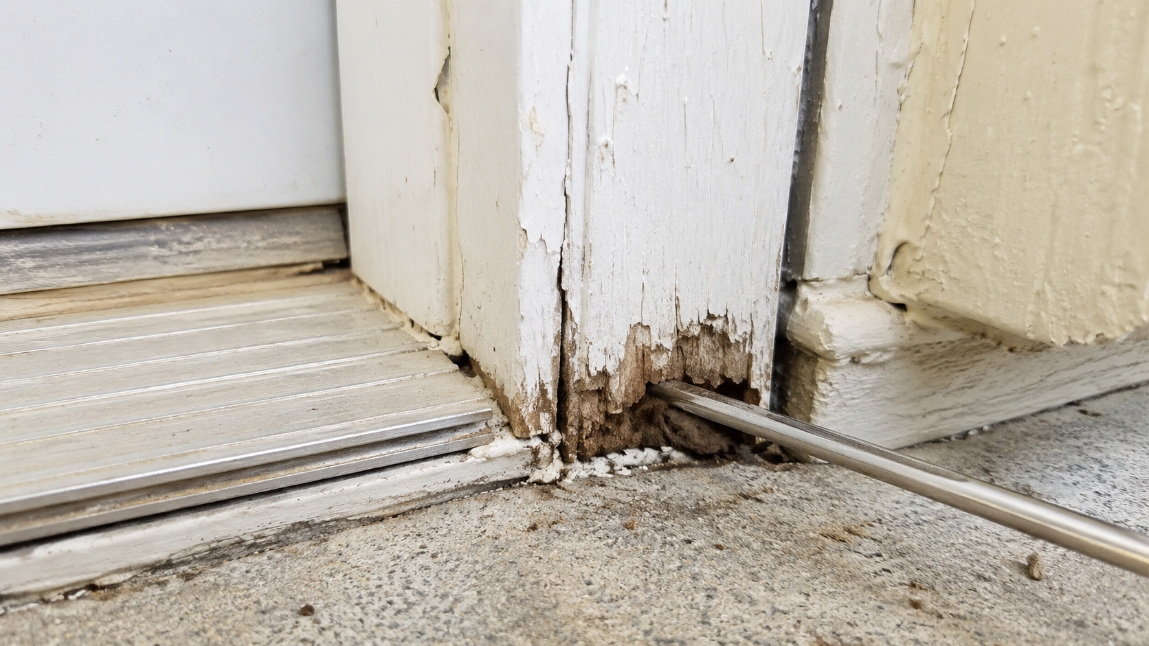 Tool checking rot at the bottom of an exterior door jamb.