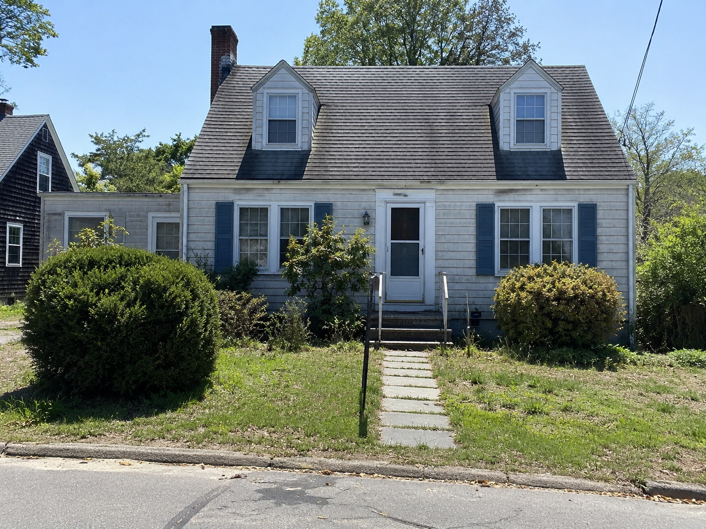 Modest Cape Cod house with two dormers, central entry, shutters, and simple front yard.