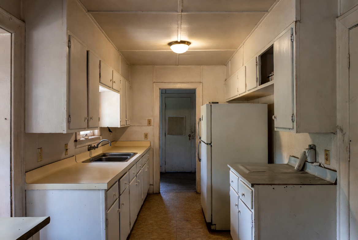 Old narrow ranch kitchen with white cabinets, low ceiling, and tight appliance layout.