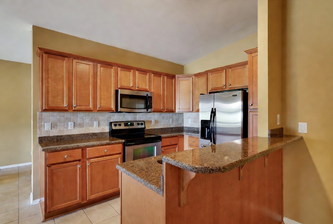 2000s kitchen with raised two-tier breakfast bar, maple cabinets, granite counters, and tile floor.