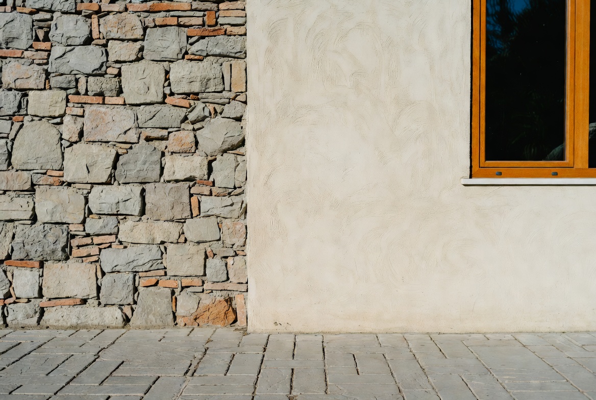 Stone wall, smooth plaster, wood-framed glass, and paving showing material texture.