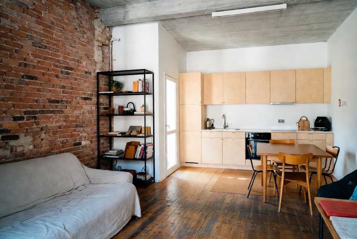 Scandinavian industrial kitchen and living room with exposed brick, wood cabinets, concrete ceiling, and warm wood floor.