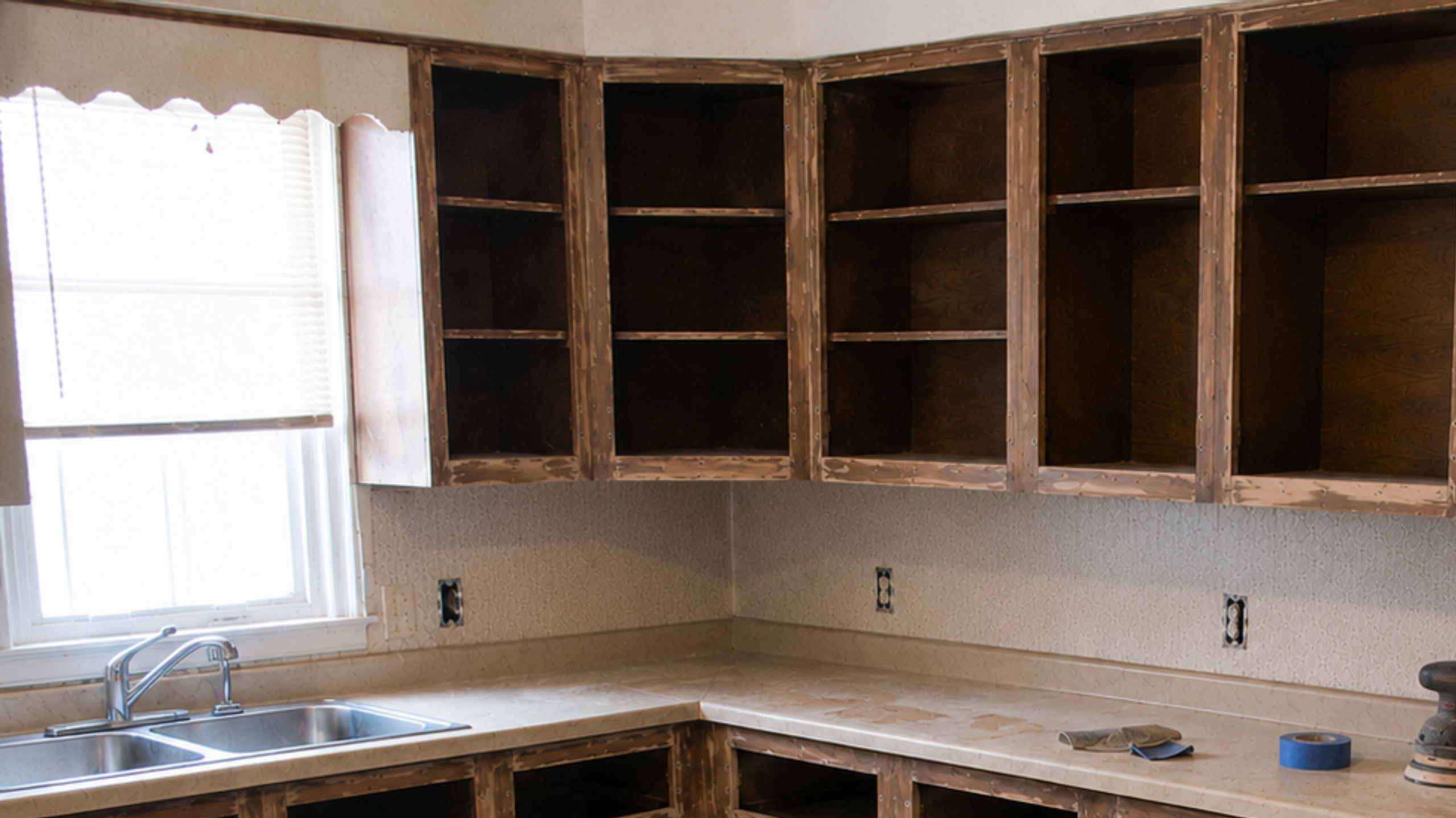 Old 1970s cabinet door being sanded with hardware holes, dust, screwdriver, and sanding sponge visible.