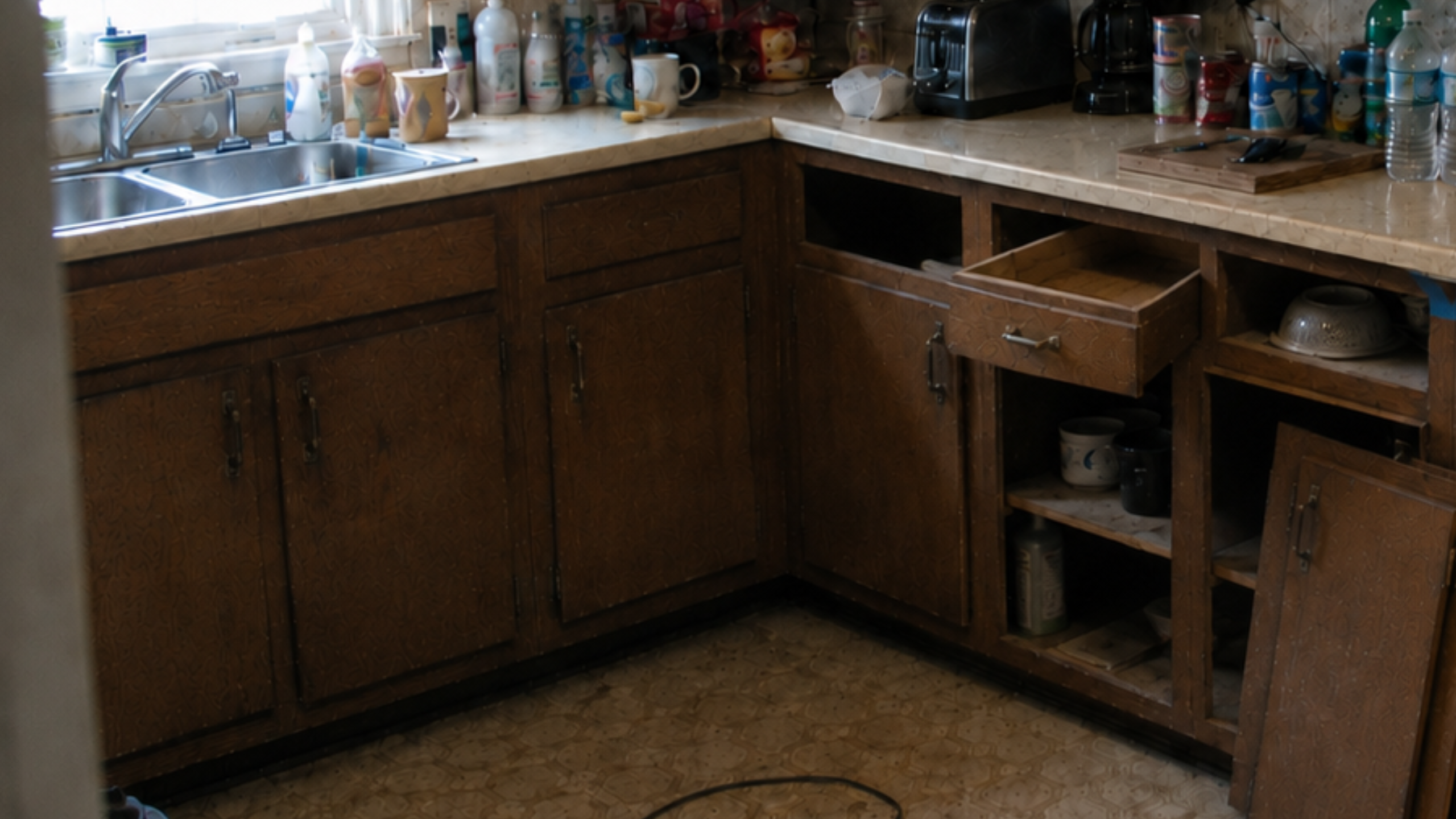 Same 1970s kitchen with cabinet doors and drawers removed, boxes exposed, and work underway.