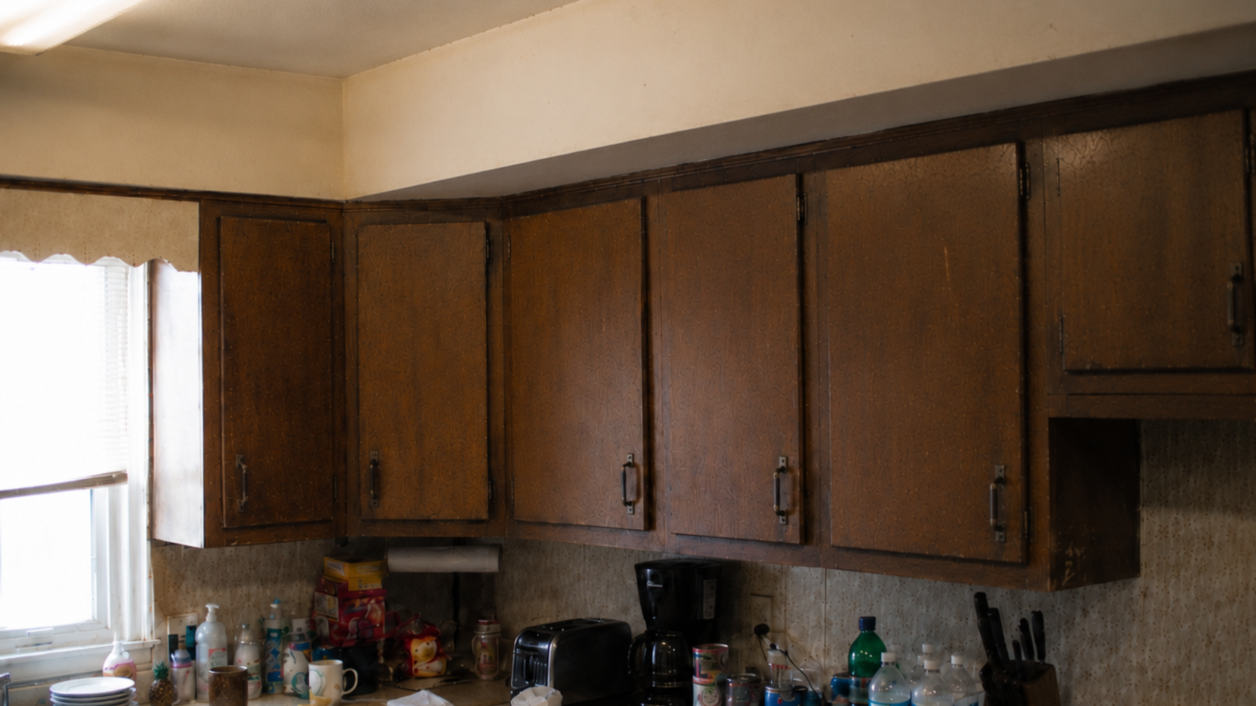 Old 1970s kitchen upper cabinets and soffit making the room feel low, dark, and boxed in.