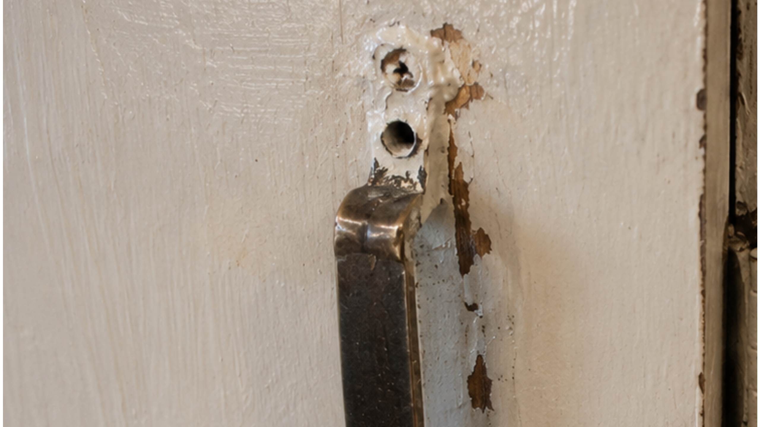 Bad paint job on an old 1970s kitchen cabinet with chipped paint, dirty hinge, rough edges, and old screw holes.