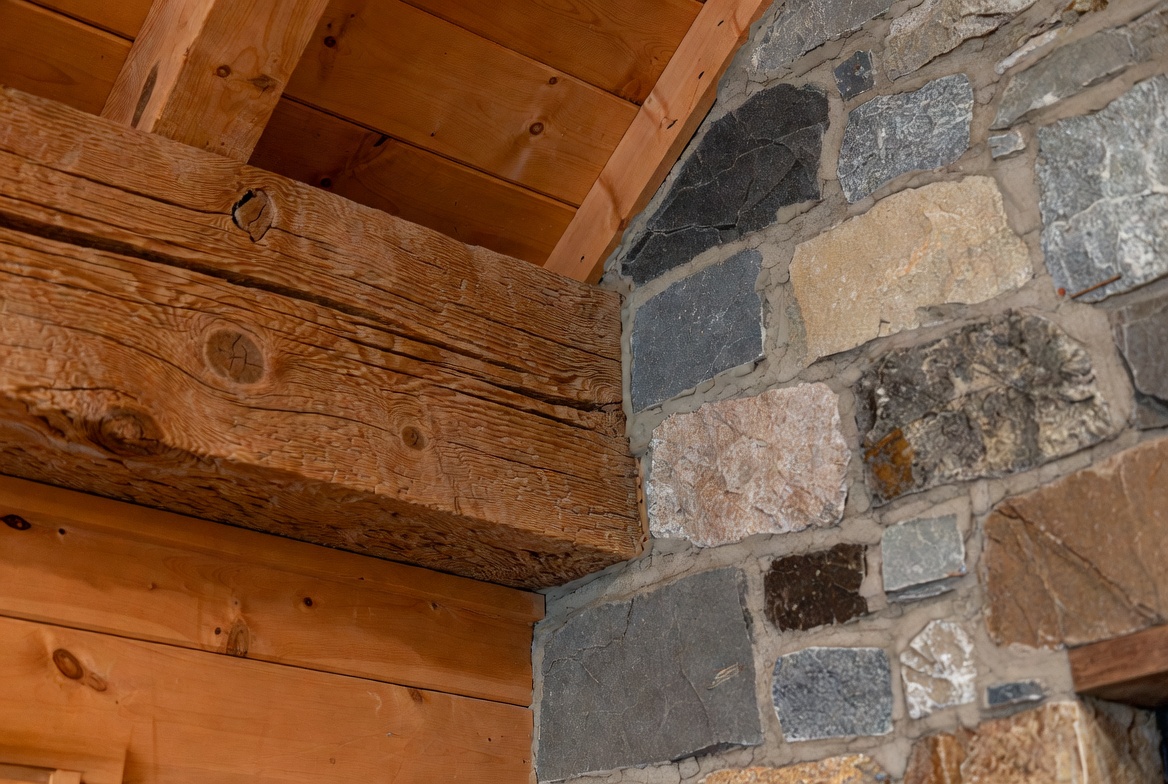 Close-up of rustic wood beam meeting stone chimney inside a house.