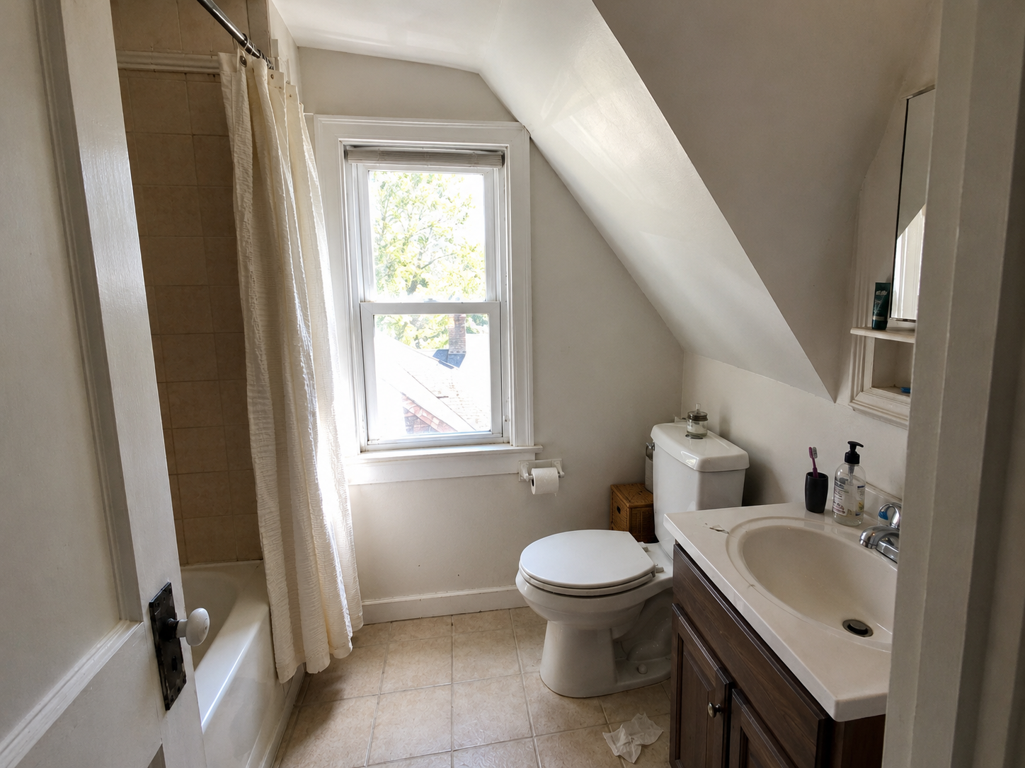 Cape Cod upstairs bathroom with sloped ceiling, window light, toilet, tub, and tight vanity.
