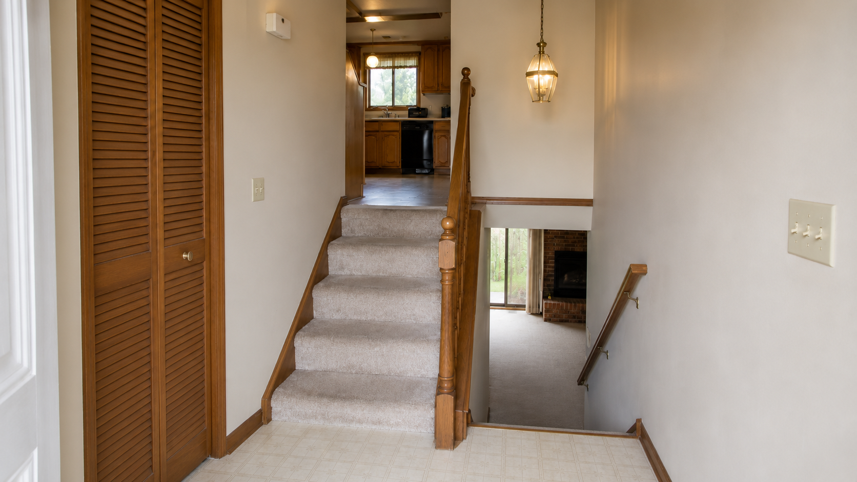 Dated split-level entry with carpeted stairs, a narrow landing, wood railings, and a louvered coat closet.
