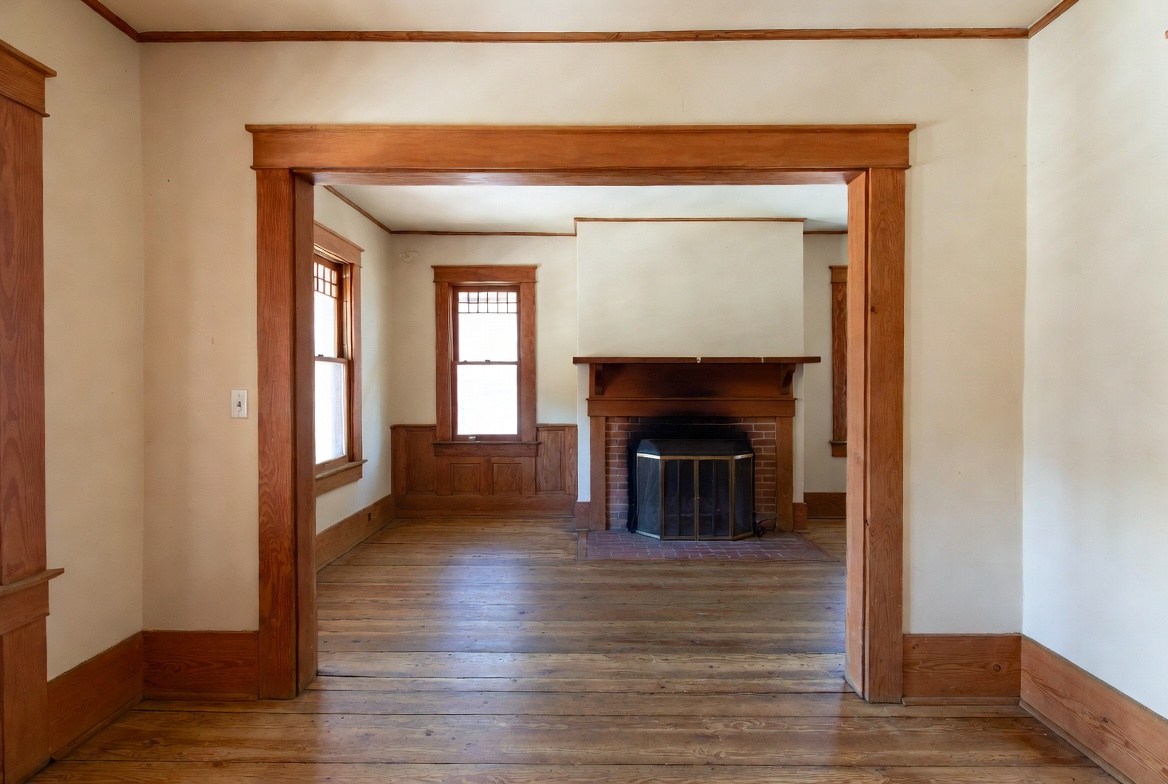 Empty Craftsman room with wood trim, fireplace, and worn hardwood floors.