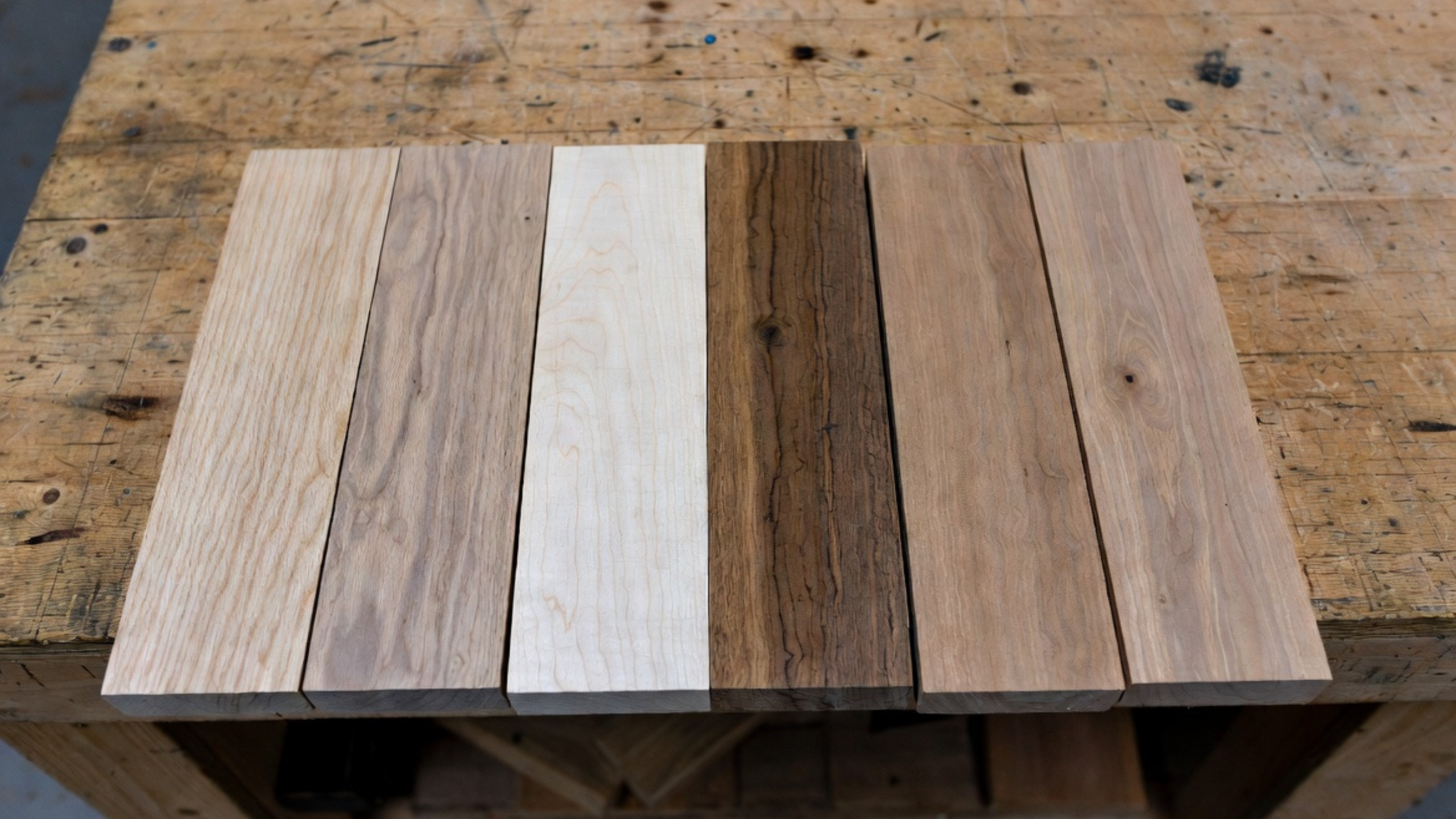 Six unfinished hardwood samples on a worn cabinetmaker’s bench.
